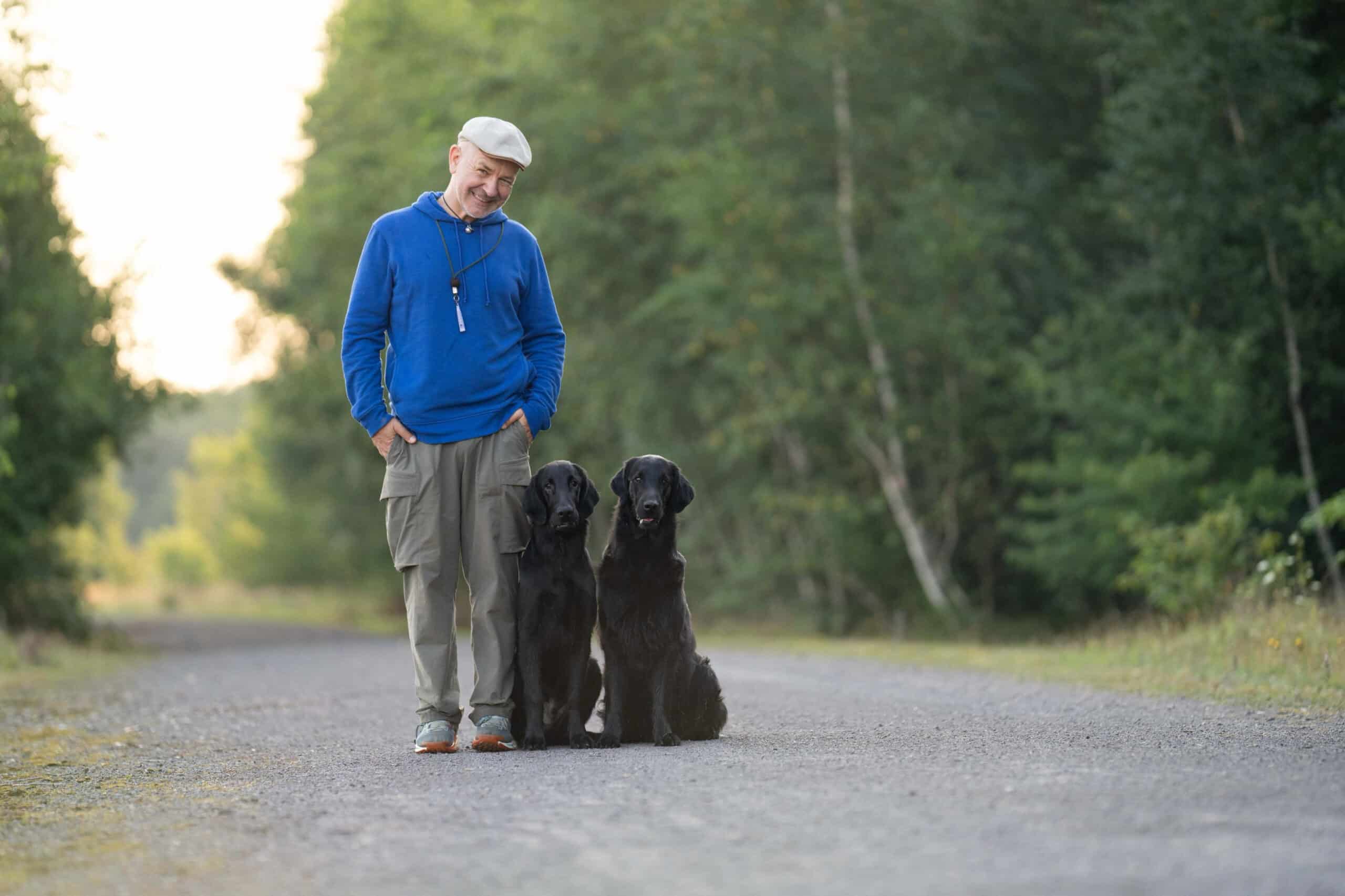 Man standing outdoors with two black dogs